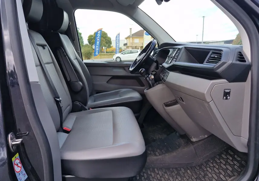 Vue intérieure côté conducteur du Volkswagen Transporter noir 2020, montrant sièges gris et tableau de bord moderne.
