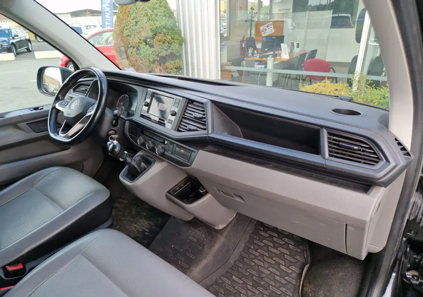 Vue intérieure côté conducteur du Volkswagen Transporter noir 2020, avec tableau de bord moderne et boîte manuelle.