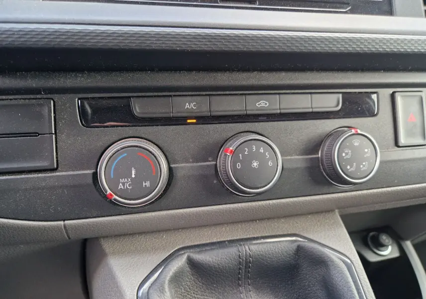 Détail du tableau de bord du Volkswagen Transporter noir 2020, montrant les commandes de climatisation manuelle et la boîte de vitesses.