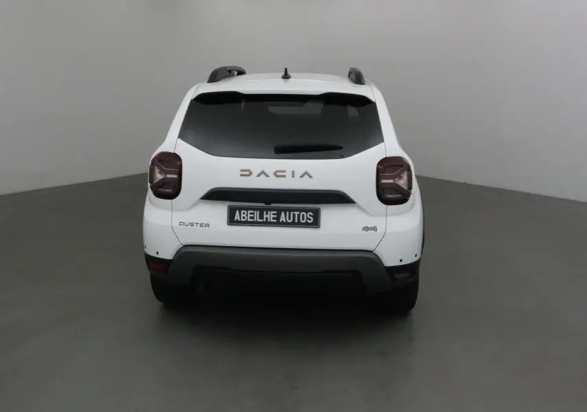 Vue arrière d'un Dacia Duster blanc 4x4 2024 avec logo DACIA et plaque Abeilhe Autos visible.