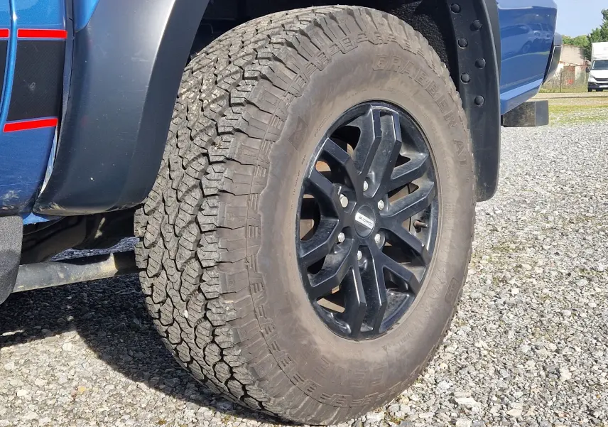 Gros plan sur la roue avant droite du Ford Ranger Raptor bleu Ford Performance, mettant en valeur la jante noire et le pneu tout-terrain.