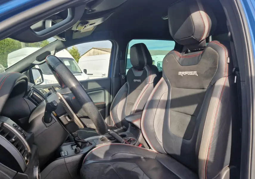Vue intérieure côté conducteur du Ford Ranger Raptor 2022, sièges en cuir noir avec surpiqûres rouges et logo Raptor brodé.