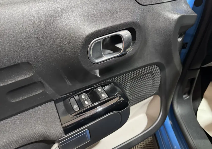 Gros plan sur la porte avant gauche d'une Citroën C3 bleu, montrant la poignée intérieure et les commandes des vitres électriques.