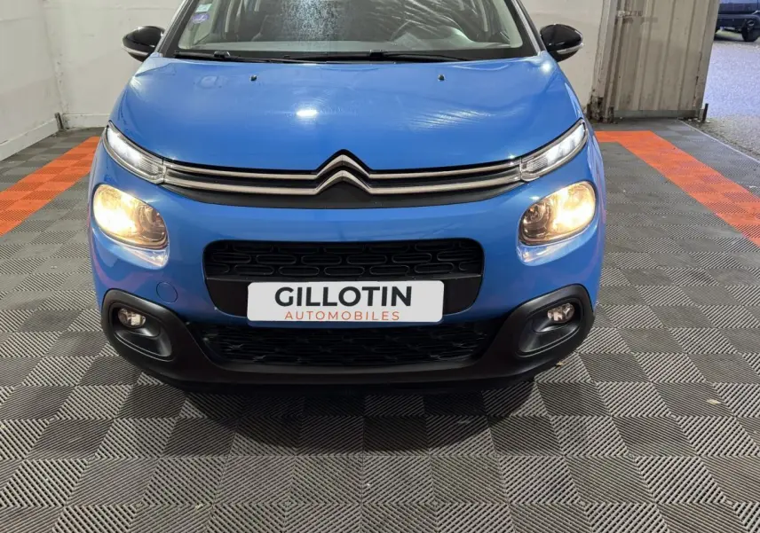 Vue frontale d'une Citroën C3 bleue 2018 avec phares allumés et logo distinctif sur calandre noire.