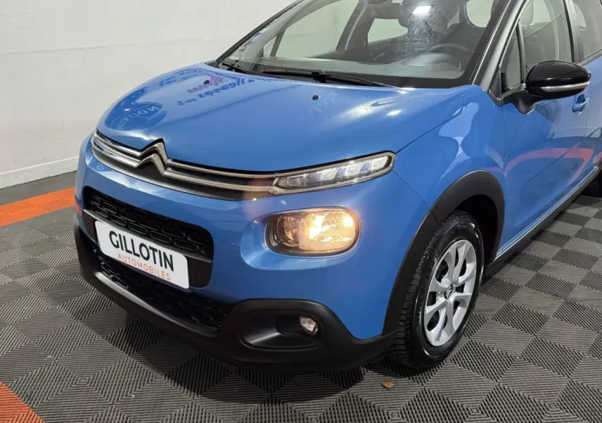 Vue 3/4 avant droite d'une Citroën C3 bleu avec phares allumés et calandre chromée distinctive.