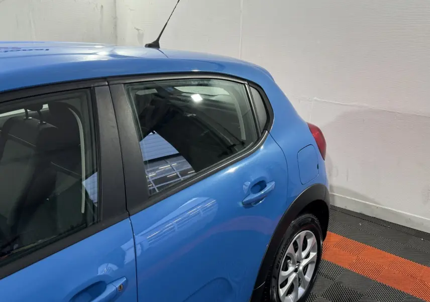 Vue latérale arrière droite d'une Citroën C3 bleu vif avec poignées et jantes visibles sur fond intérieur.
