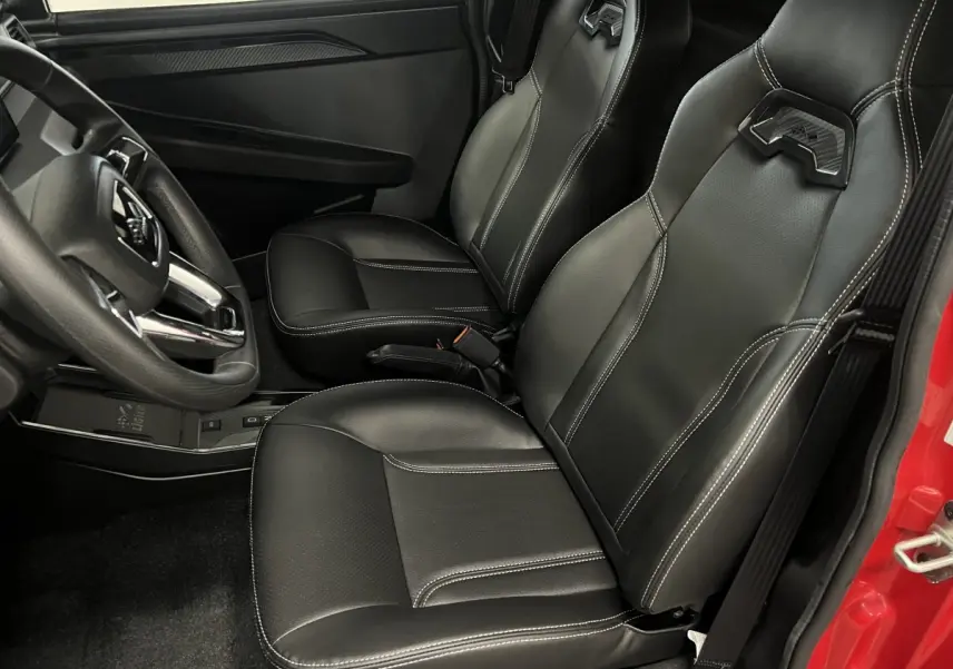 Vue intérieure côté conducteur montrant les sièges noirs en cuir avec surpiqûres blanches et partie de la portière rouge.
