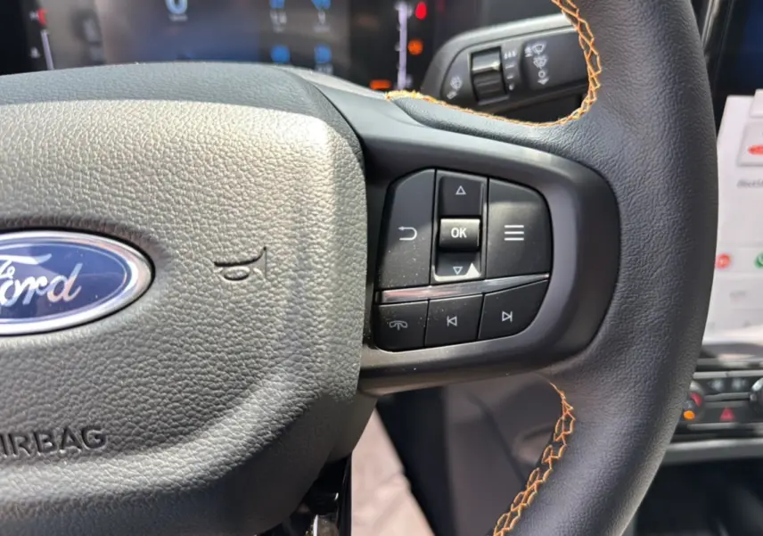 Gros plan sur le volant en cuir noir avec surpiqûres orange du Ford Ranger 2025, boutons multifonctions visibles.