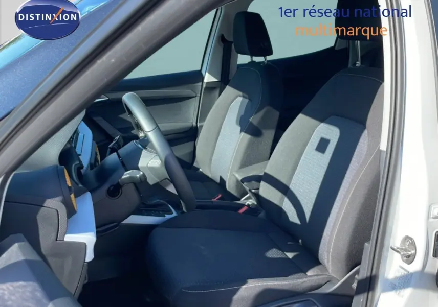 Vue intérieure côté conducteur du SEAT Arona blanc, montrant les sièges tissu noir et gris et le volant multifonction.