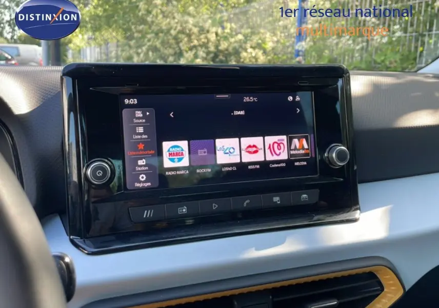 Gros plan sur l’écran tactile central du tableau de bord d’un SEAT Arona blanc avec toit gris, affichant les options radio.