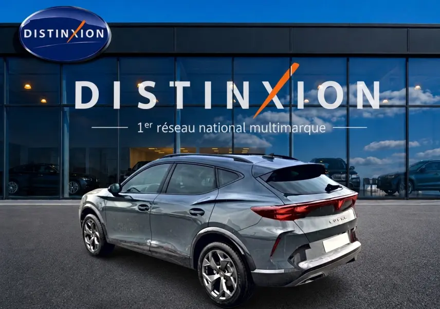 Vue 3/4 arrière droite d'une CUPRA Formentor bleu fjord avec feux arrière LED et jantes 18 pouces devant un showroom Distinxion.