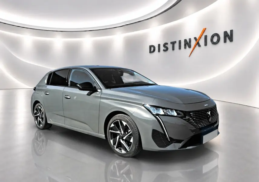 Peugeot 308 gris vue 3/4 avant droit, jantes alu noires et phares LED dans un showroom lumineux.