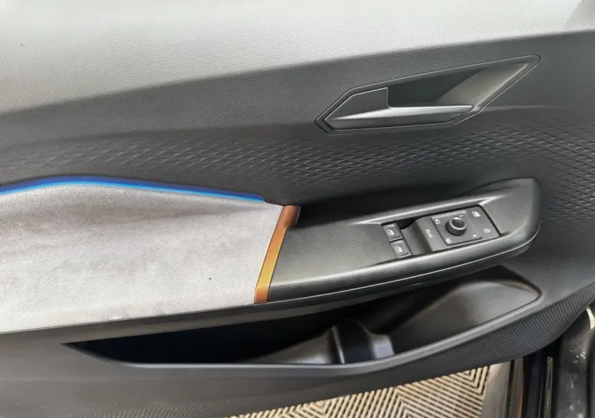 Vue intérieure côté gauche de la porte d’une CUPRA Born 230ch gris foncé avec insert bleu et commandes de vitres.