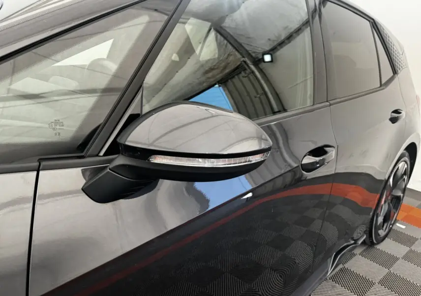 Gros plan sur le rétroviseur côté gauche et la portière gris foncé d'une CUPRA BORN 230ch, reflet du plafond visible.