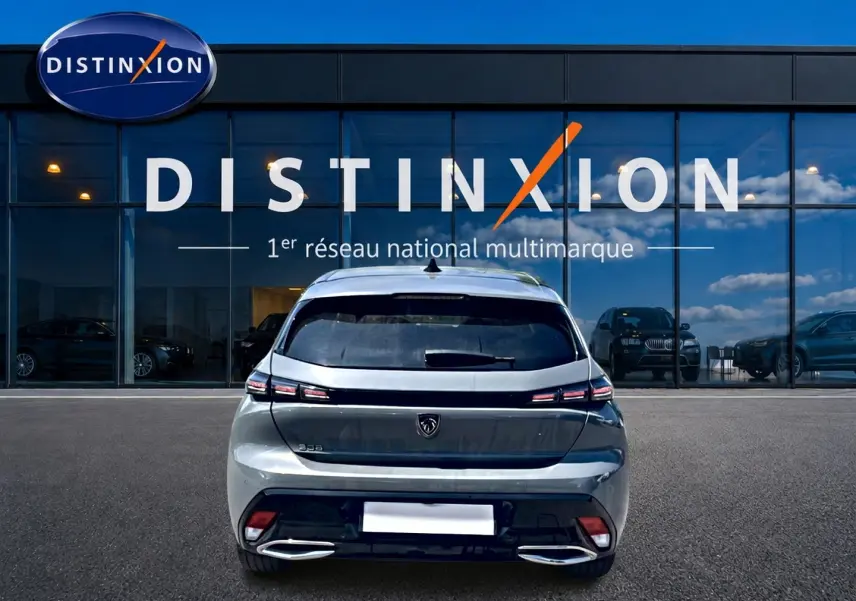 Vue arrière d'une Peugeot 308 gris 2025 garée devant une vitrine avec logo Distinxion.