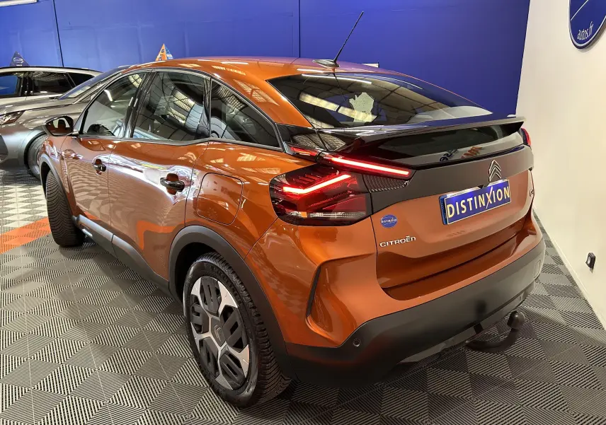 Vue 3/4 arrière droite d'une Citroën C4 orange 2021 avec attelage et feux arrière LED allumés en intérieur showroom.