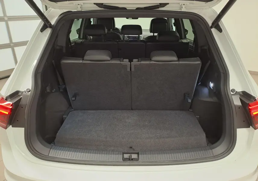 Coffre ouvert vu de l'arrière d'un Volkswagen Tiguan Allspace blanc pur, montrant la troisième rangée de sièges relevée.