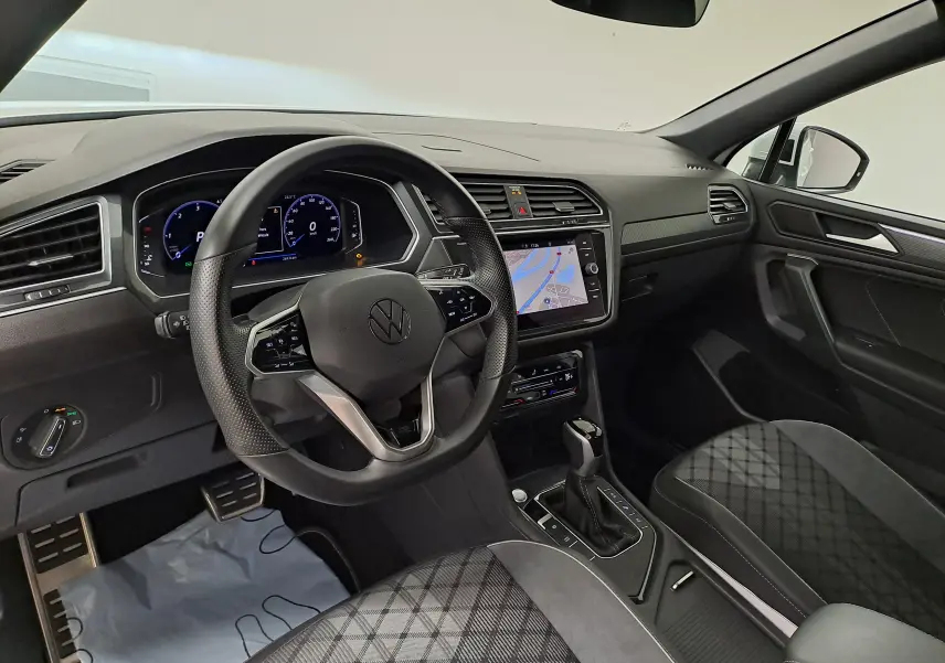 Intérieur du Volkswagen Tiguan Allspace R-Line 2023 vu côté conducteur, avec tableau de bord numérique et sellerie noire à motifs.