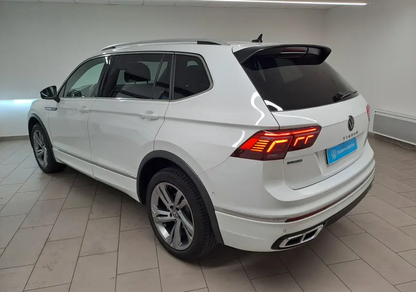 Volkswagen Tiguan Allspace blanc pur en 3/4 arrière droit, feux arrière allumés et finition R-Line visible.