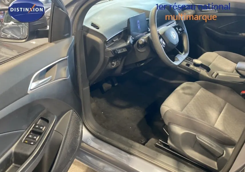 Vue intérieure côté conducteur de la MG3 1.5 Hybrid 2024 en gris Hampstead, montrant le tableau de bord et les sièges tissu gris.