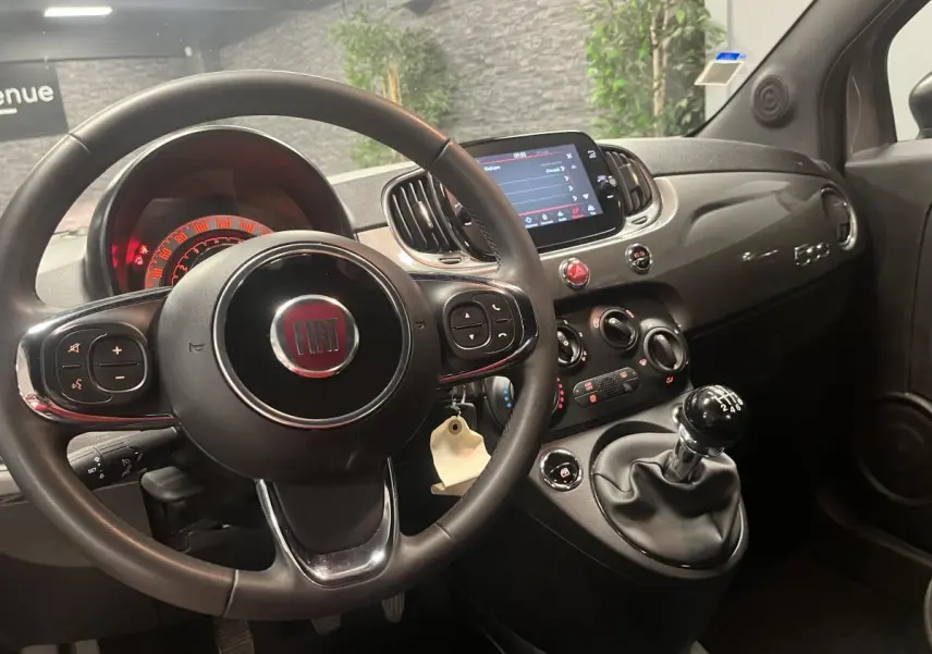 Intérieur noir de la Fiat 500 2023, vue du poste de conduite avec volant, tableau de bord et levier de vitesses manuel.