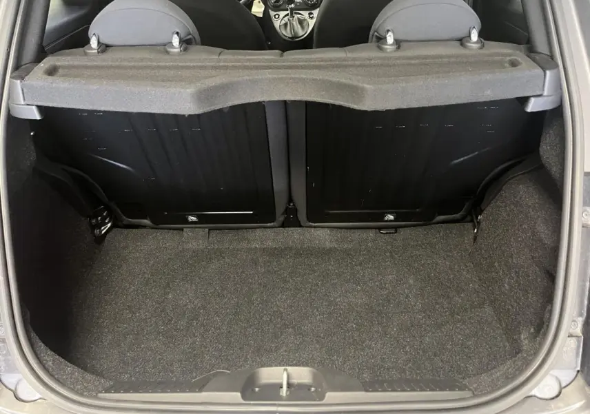 Coffre ouvert vu de l'arrière d'une Fiat 500 gris, montrant la banquette arrière rabattable et le tapis de coffre.
