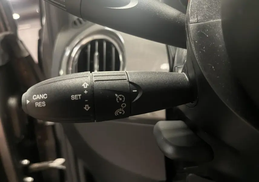 Gros plan sur la commande de régulateur de vitesse noire à gauche du volant dans l'habitacle d'une Fiat 500 gris 2023.