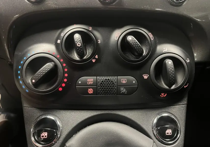 Gros plan sur les commandes de climatisation manuelle et vitres électriques de la Fiat 500 gris métallisé 2023.
