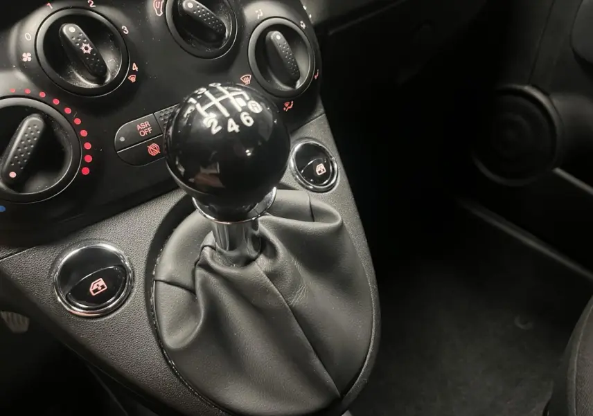 Le levier de vitesses manuel noir et les commandes de climatisation du tableau de bord d'une Fiat 500 gris 2023.