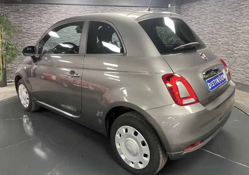 Fiat 500 gris métallisé vue 3/4 arrière droit, avec jantes acier et poignées de porte chromées.