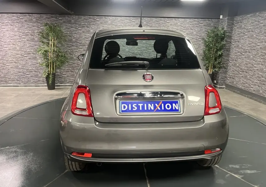 Vue arrière d'une Fiat 500 hybride gris métallisé avec logo Fiat et plaque Distinxion en intérieur showroom.