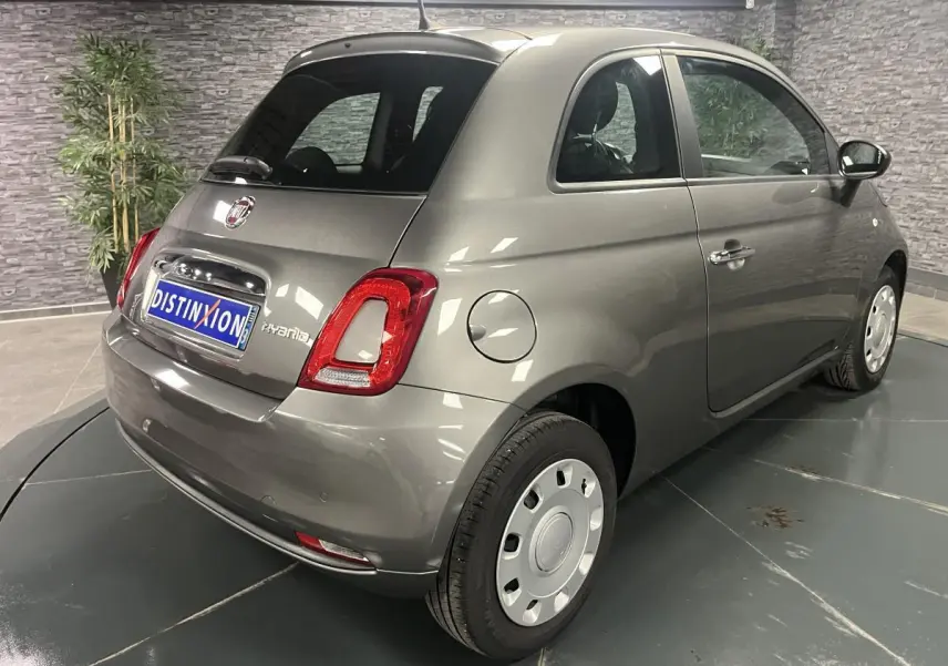 Vue 3/4 arrière droite d'une Fiat 500 hybride gris métallisé avec jantes acier et feux arrière LED dans un showroom.