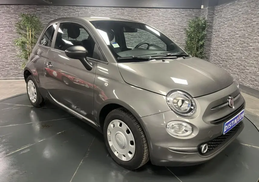 Fiat 500 gris métallisé vue 3/4 avant droit avec jantes acier et rétroviseurs noirs dans un showroom.