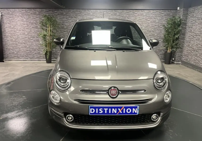 Vue avant d'une Fiat 500 gris métallisé avec projecteurs ronds et calandre chromée en intérieur showroom.