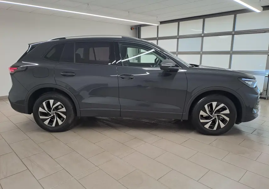 Vue de profil côté gauche du Volkswagen Tiguan 2024 gris Urano avec crochet d'attelage escamotable en intérieur showroom.