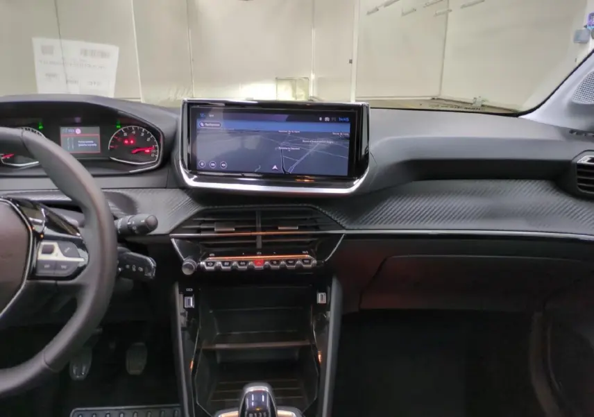 Vue intérieure avant du tableau de bord de la Peugeot 208 2025, avec écran tactile 10 pouces et volant cuir noir.