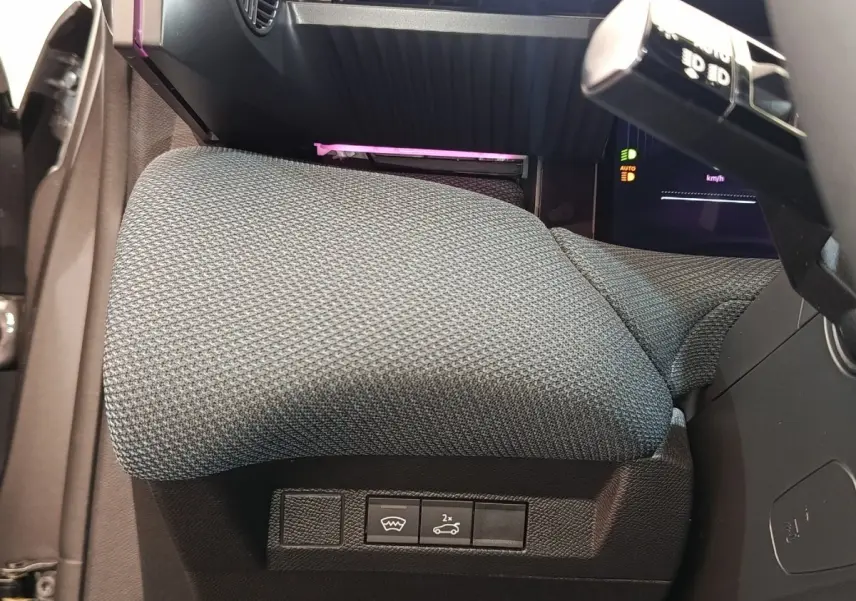 Gros plan sur l'accoudoir central gris et les commandes sous le volant du Citroën C5 hybride 2025.