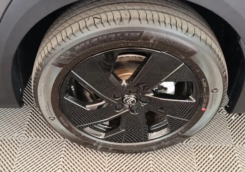 Gros plan sur la roue avant droite noire brillante avec logo Citroën sur un Citroën C5 gris foncé.