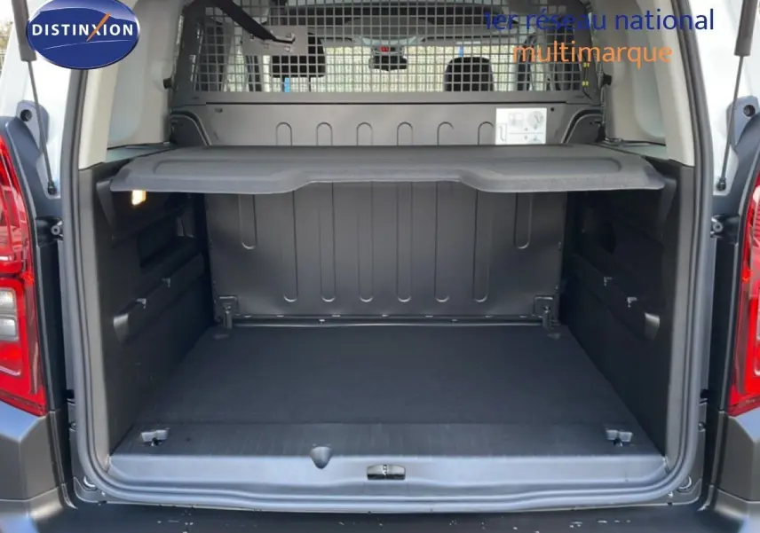 Coffre ouvert vu de l'arrière d'un Citroën Berlingo blanc glacier 2025 avec séparation grillagée et tablette de rangement.