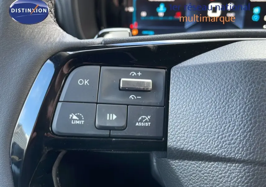 Gros plan sur les commandes au volant noir d’un Citroën Berlingo blanc glacier, avec affichage numérique en arrière-plan.