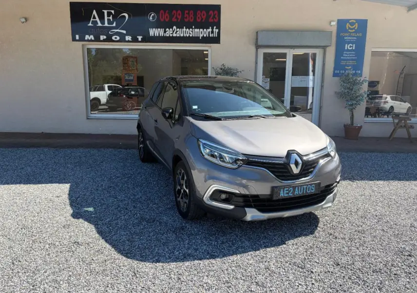 Renault Captur gris 3/4 avant droit, jantes alliage et calandre noire, stationné devant un garage AE2 Autos.