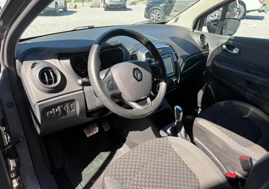 Vue intérieure côté conducteur du Renault Captur gris 2017, volant multifonctions, écran tactile et levier de boîte auto visibles.