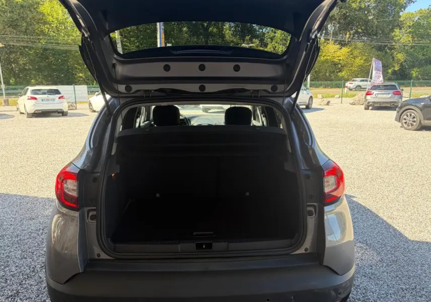 Vue arrière ouverte sur le coffre d'un Renault Captur gris 2017, montrant l'espace de chargement et les feux arrière.