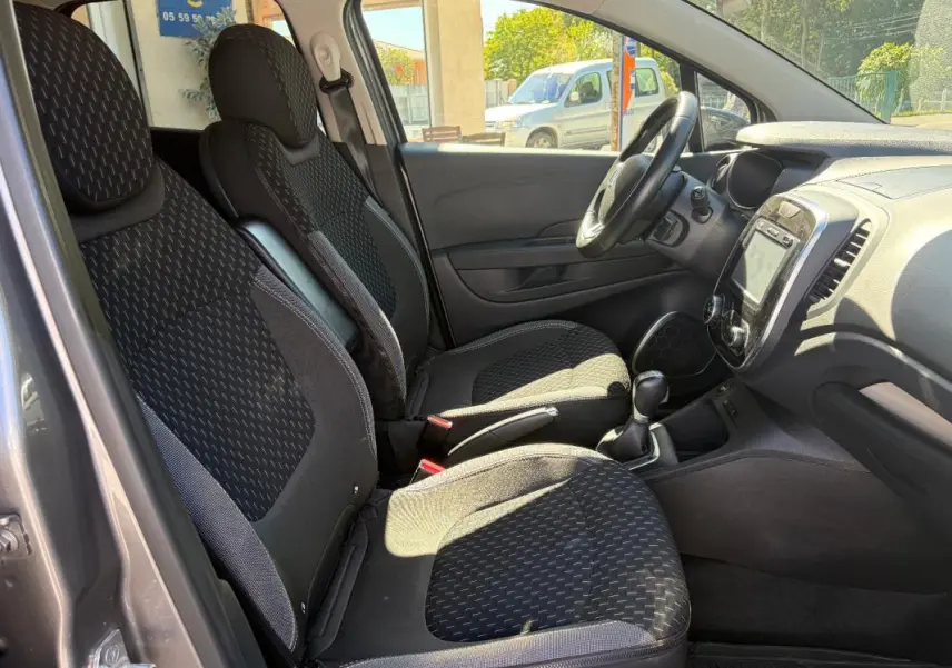 Vue intérieure côté conducteur du Renault Captur gris 2017, montrant sièges tissu, volant multifonctions et écran tactile central.