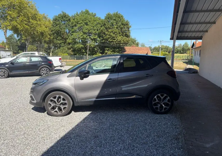 Vue de profil côté gauche d'un Renault Captur gris 2017 avec jantes alliage, stationné sur un sol gravillonné.