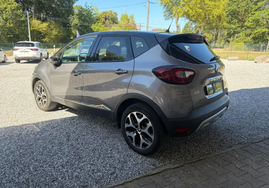 Renault Captur gris 3/4 arrière droit, jantes alliage et vitres teintées sous un ciel ensoleillé.