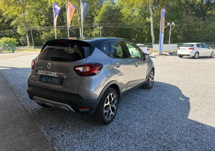 Renault Captur gris 3/4 arrière droit, jantes alliage et toit noir contrasté sur parking ensoleillé.