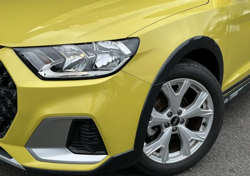 Gros plan sur l'avant droit d'une Audi A1 Allstreet jaune Python, mettant en valeur le phare et la jante en aluminium.