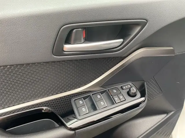 Gros plan sur la commande des vitres et la poignée intérieure côté conducteur d’un Toyota C-HR Hybride blanc toit noir.