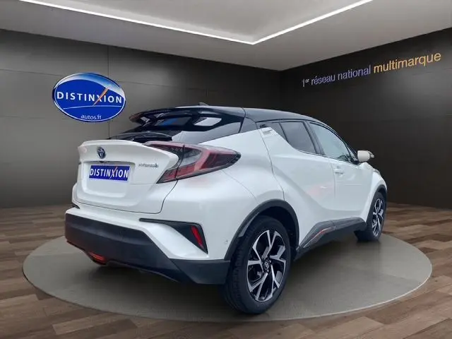 Vue 3/4 arrière droite du Toyota C-HR Hybride blanc toit noir, soulignant ses lignes anguleuses et ses jantes alliage noires.